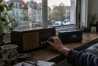 Old and modern tabletop radios beside a window, with a listener adjusting the analog tuning dial.